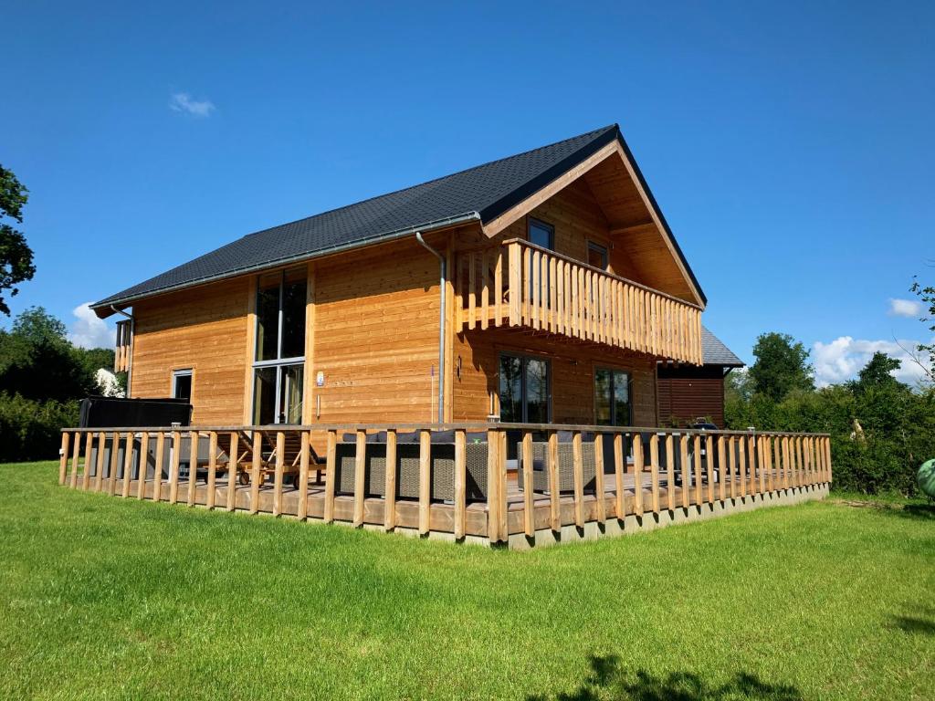 a log cabin with a wooden fence in the grass at Chalet Colorado - jacuzzi, playstation in Durbuy