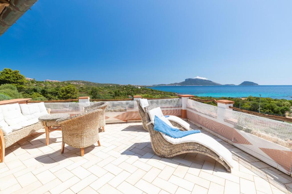 d'une terrasse avec des chaises et des tables en osier et l'océan. dans l'établissement Costa Smeralda Holiday Apartments, à Golfo Aranci