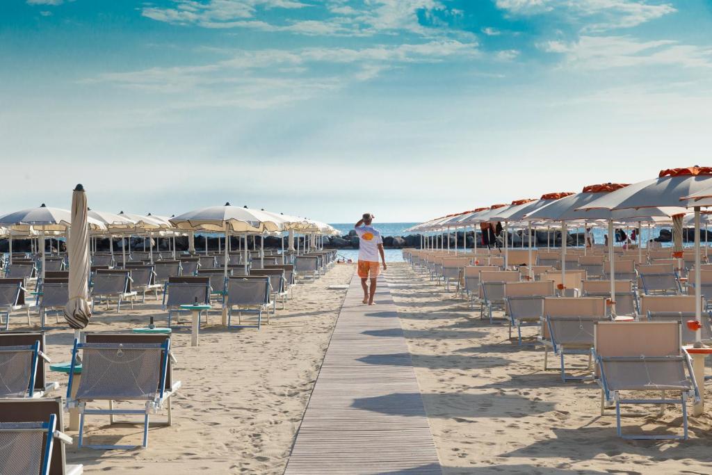 Eine Frau, die am Strand mit Stühlen und Sonnenschirmen spazieren geht in der Unterkunft Hotel Castellucci in Bellaria-Igea Marina