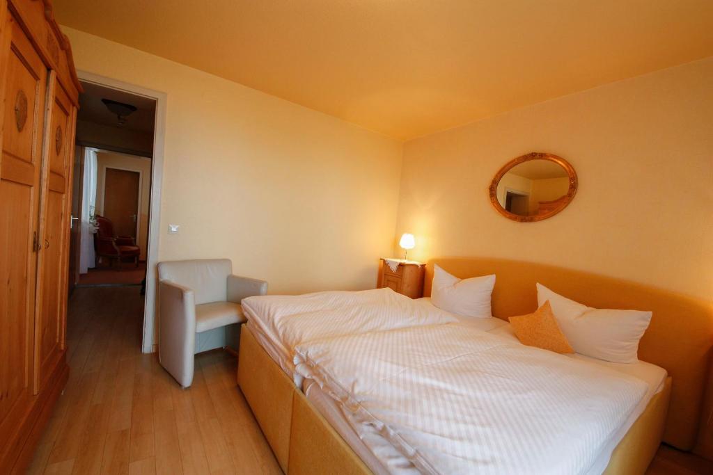 ein Schlafzimmer mit einem Bett mit einem Spiegel und einem Stuhl in der Unterkunft Gästehaus Garni Merk in Immenstaad am Bodensee