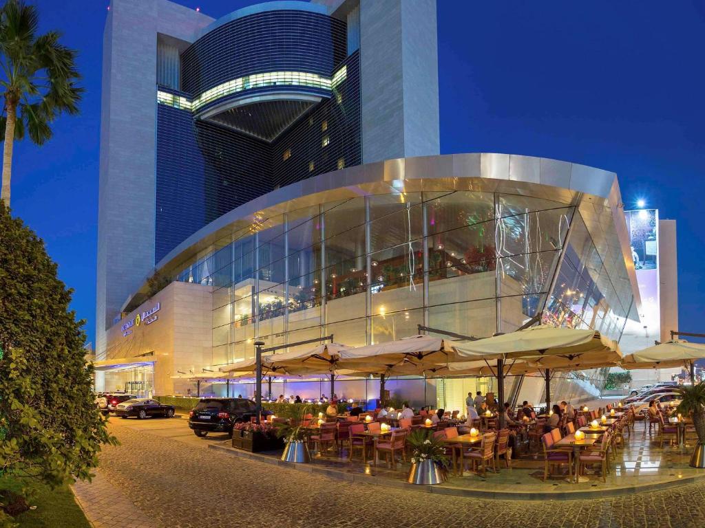 a group of people sitting at tables in front of a building at La Cigale Hotel Managed by Accor in Doha