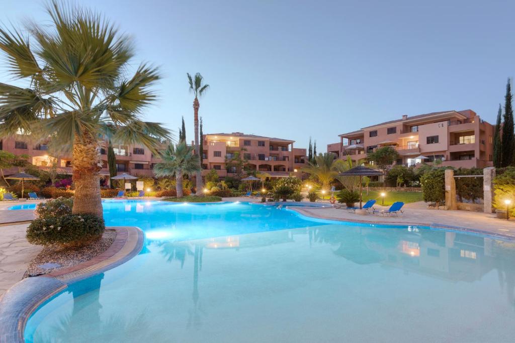 a large swimming pool with palm trees and buildings at Resitour - Aphrodite Gardens in Paphos City