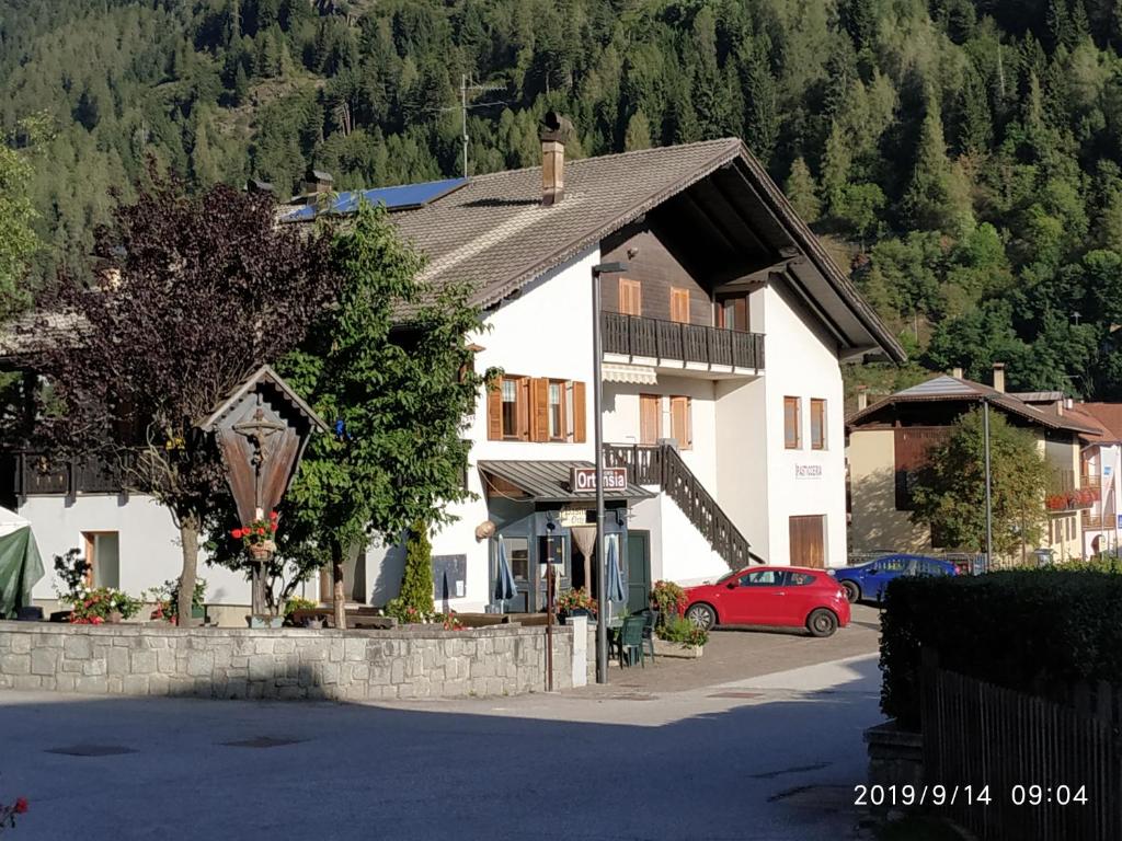 un grande edificio bianco con un'auto rossa parcheggiata di fronte di Casa Ortensia a Pellizzano