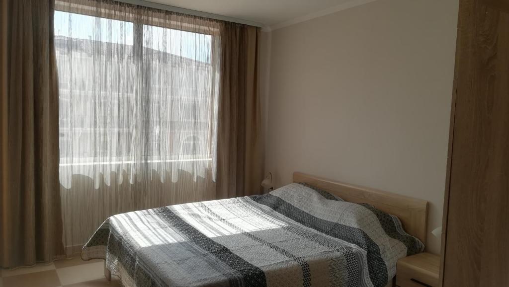 1 dormitorio con 1 cama con manta a cuadros y ventana en Hasienda Beach апартаменти, en Sozopol