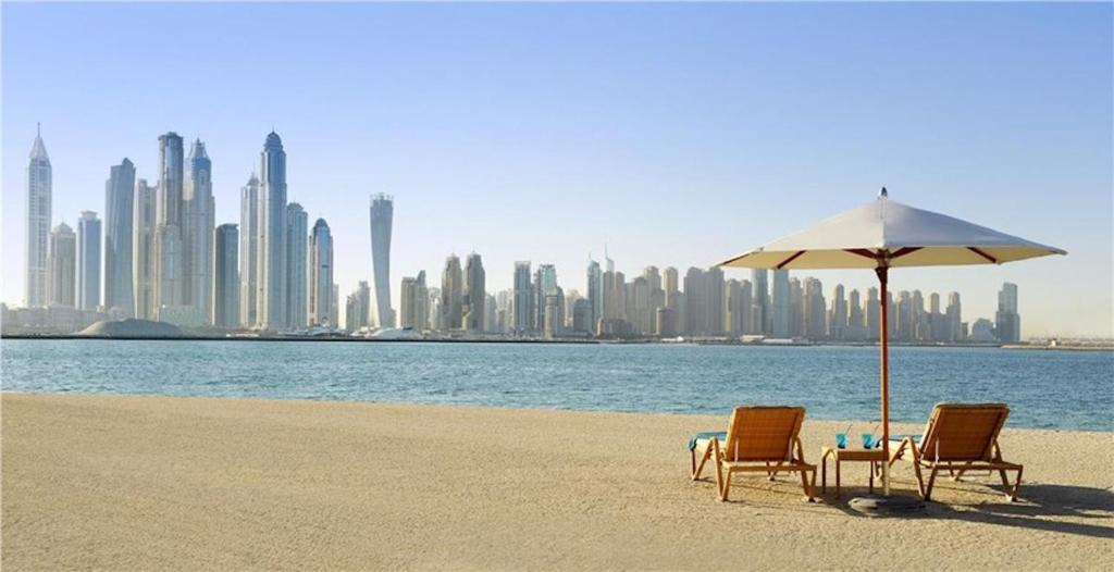 due sedie e un ombrellone su una spiaggia con una città di bnbmehomes - Beach&Pool - Fairmont Residences - 3605 a Dubai