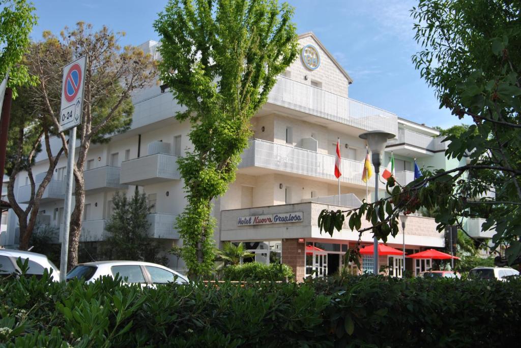 un gran edificio blanco con coches estacionados frente a él en Hotel Nuova Graziosa, en Lignano Sabbiadoro