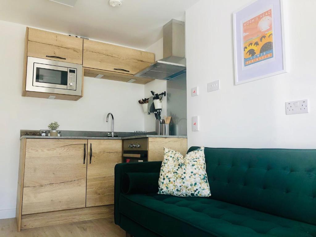 One One Five Apartment في سوانسي: غرفة معيشة مع أريكة خضراء ومطبخ