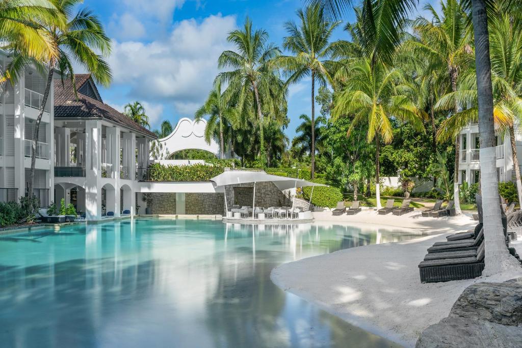 a swimming pool in front of a building with palm trees at Peppers Beach Club in Port Douglas