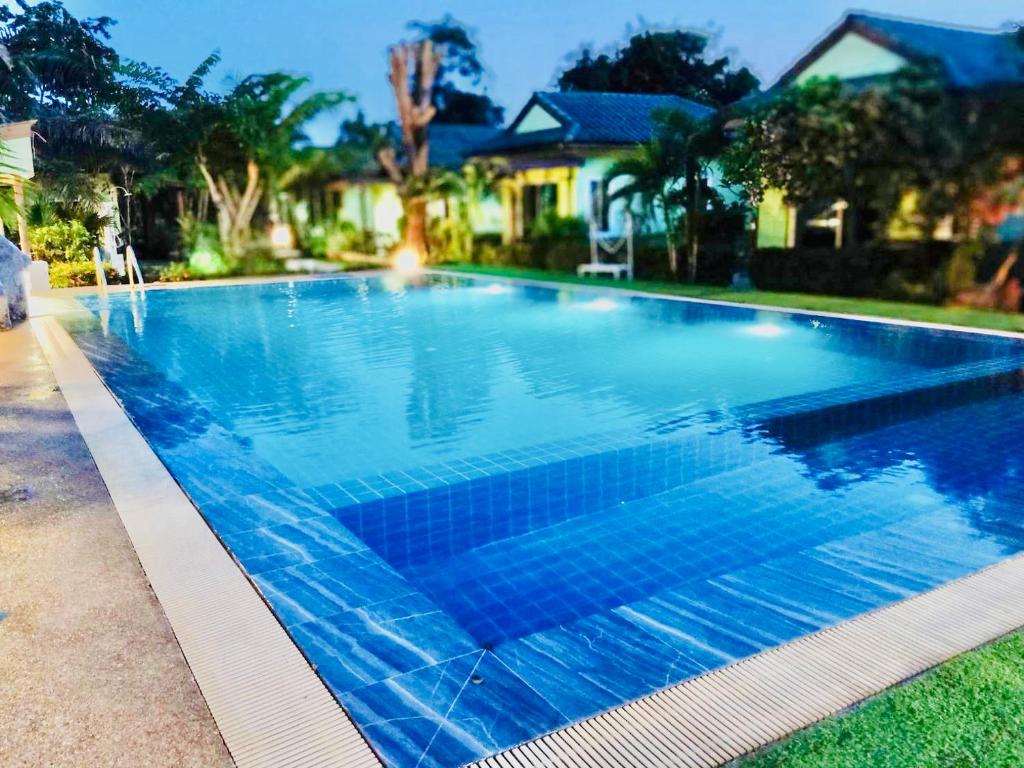 a large swimming pool with blue water in front of a house at แสงหิรัญ บีช รีสอร์ท in Pran Buri