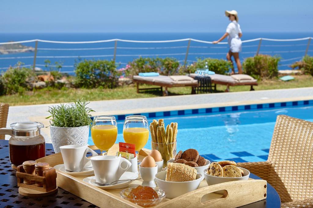 a table with breakfast food and drinks next to a swimming pool at Okeanides Villas in Balíon