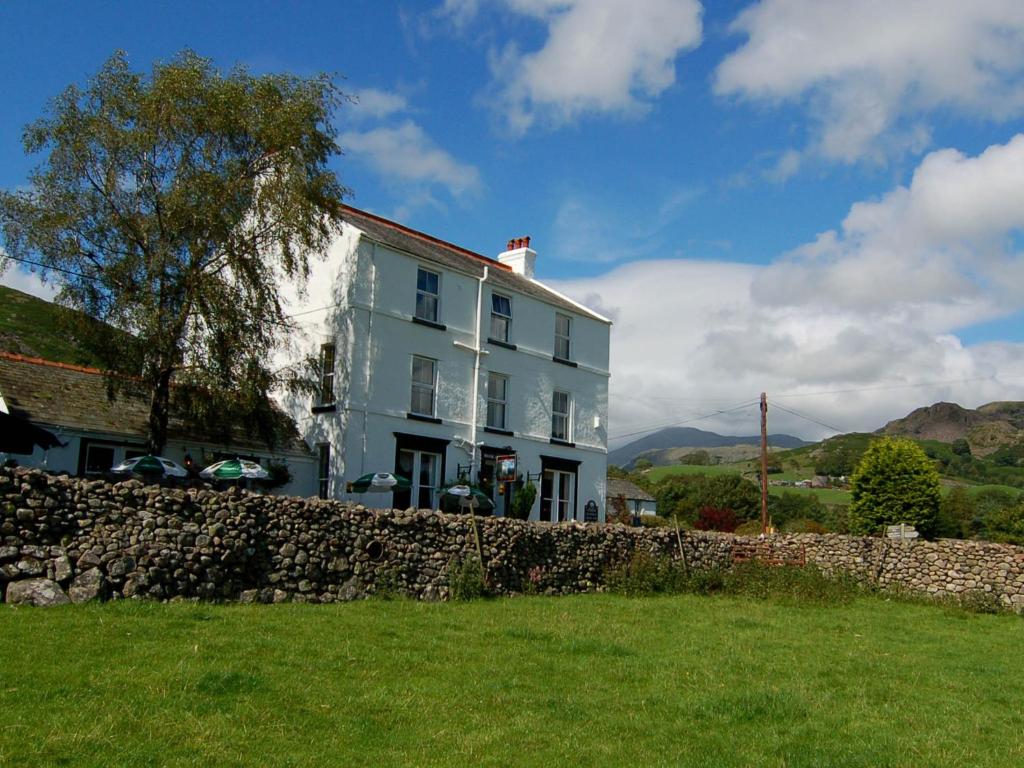 ein weißes Haus mit einer Steinmauer neben einem Gebäude in der Unterkunft Brook House Inn in Eskdale