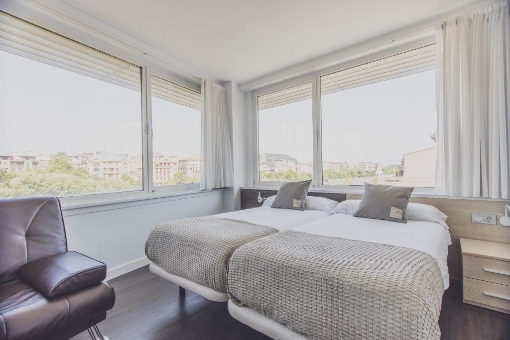 a bedroom with a bed and a chair and windows at Pensión Riberas del Urumea in San Sebastián