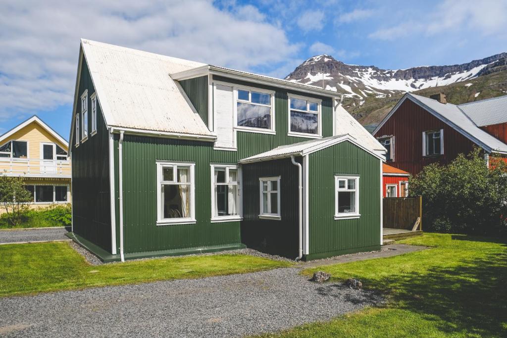a green and white house with a mountain in the background at Hotel Aldan - The Old School in Seyðisfjörður