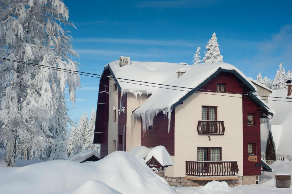 a house covered in snow next to a tree at Apartments and Rooms Planinska Idila in Jahorina