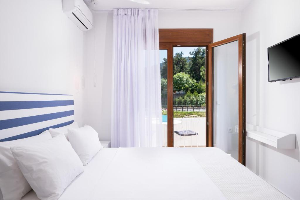 a white bedroom with a bed and a window at Villa Victoria by La Scala Beach in Limenas