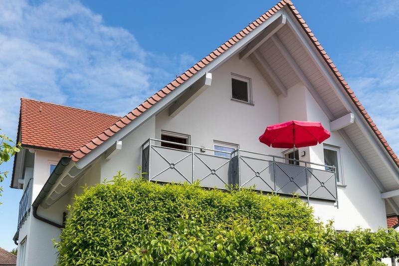 a white house with a red umbrella on a balcony at Ferienwohnung Haidle in Eriskirch