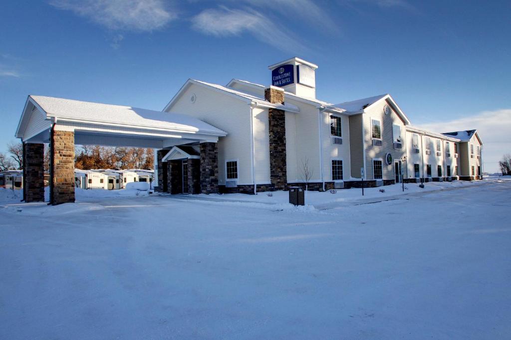 a large white building with snow in front of it at Cobblestone Inn & Suites - Rugby in Rugby