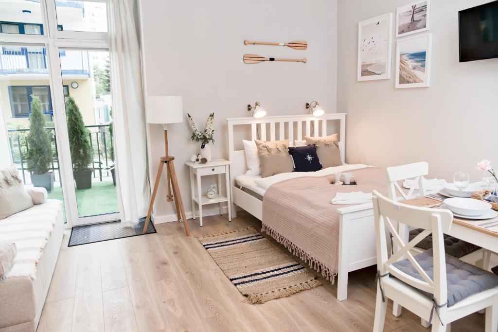 a white bedroom with a bed and a dining table at Portofino Seaside Apartments in Międzyzdroje