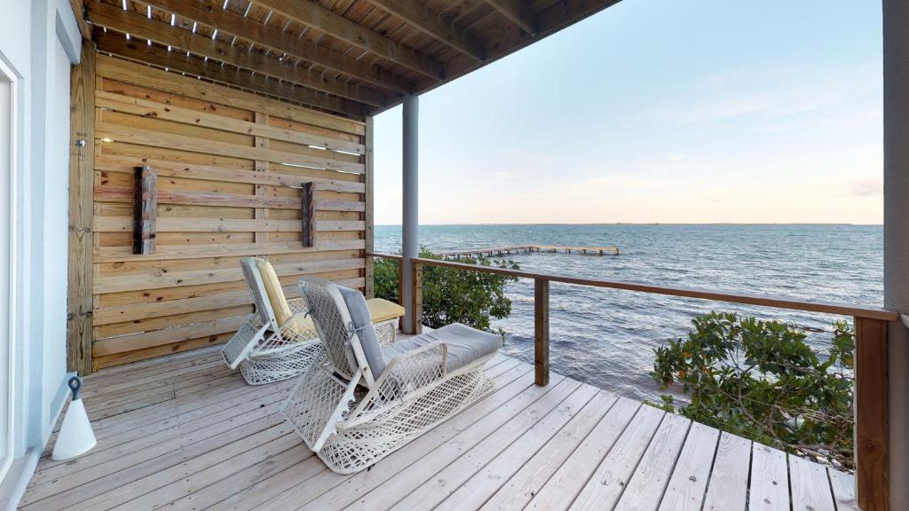 two wicker chairs sitting on a deck overlooking the ocean at Thatch Caye Resort a Muy'Ono Resort in Hopkins