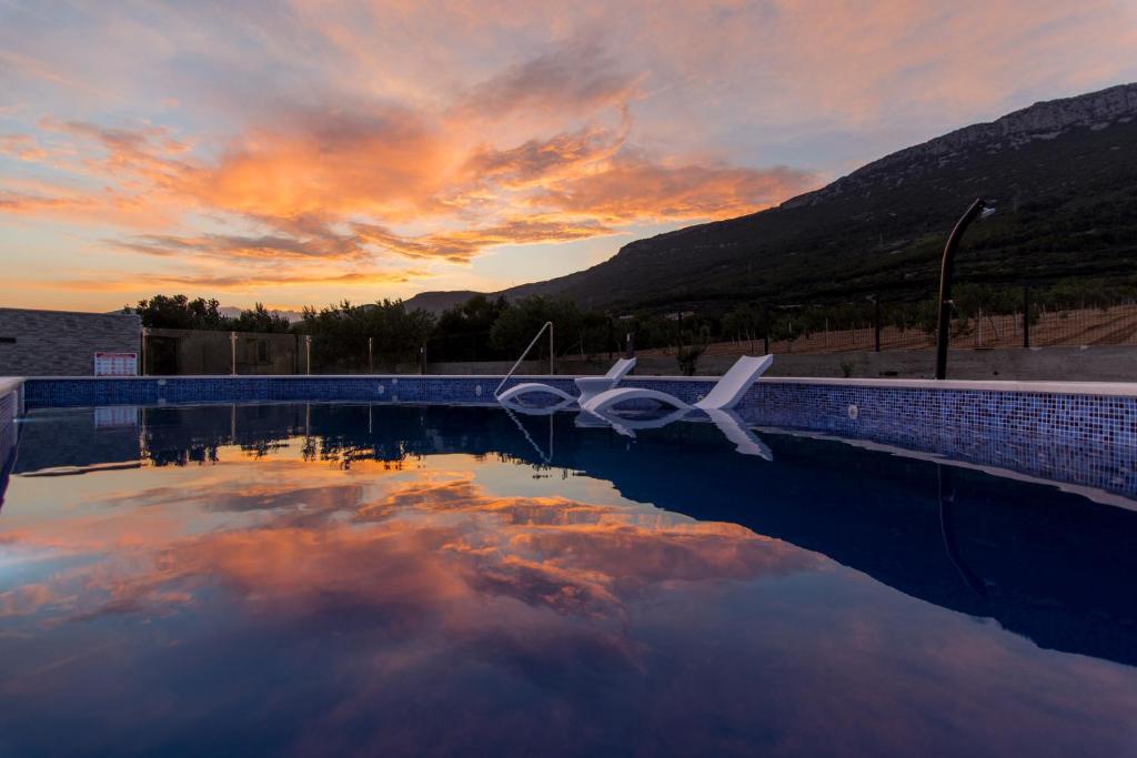 a pool with two white chairs sitting next to a sunset at Villa Olive`s secret in Kastel Luksic