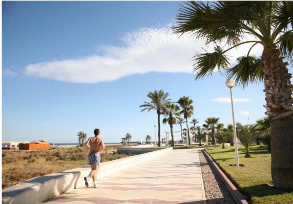 un hombre caminando por una acera junto a una palmera en Apartamento en Las Marinas Vera, en Los Amarguillos