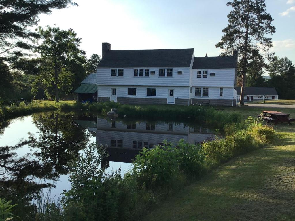 a white house with a reflection in a body of water at Stonybrook Motel & Lodge in Franconia