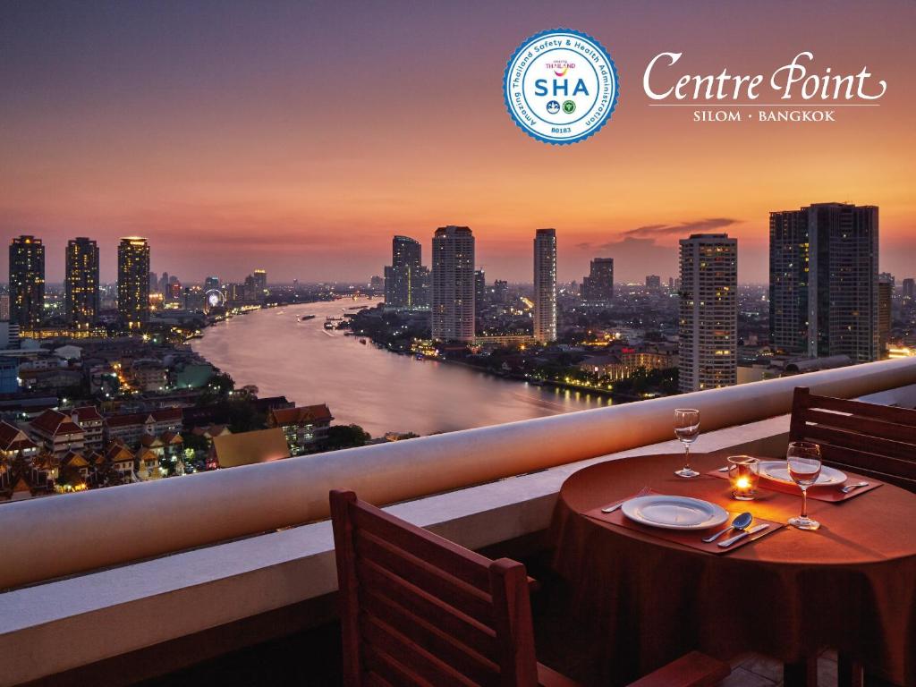 a table with wine glasses on a balcony with a view of a river at Centre Point Silom in Bangkok