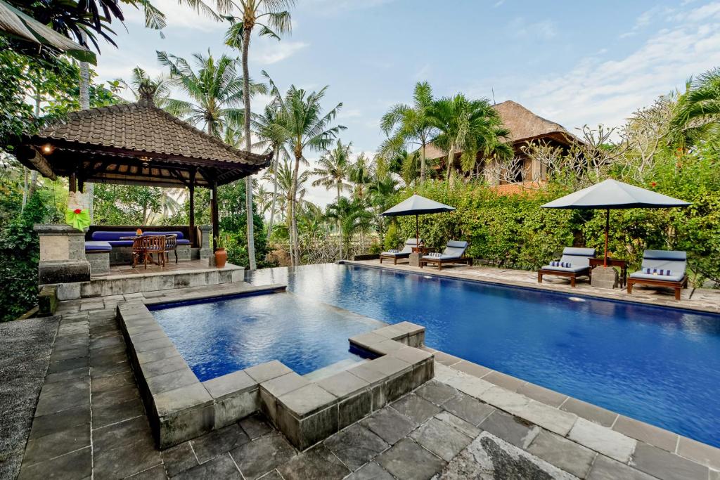 a swimming pool in a resort with chairs and umbrellas at Alam Shanti Ubud in Ubud