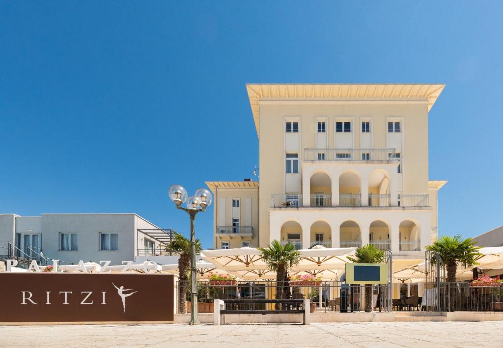 a large white building with palm trees in front of it at BO Hotel Palazzo in Poreč