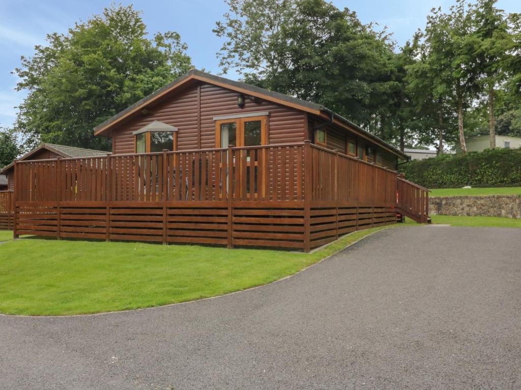 a wooden cabin with a fence and grass at Crocus Lodge in Bodmin