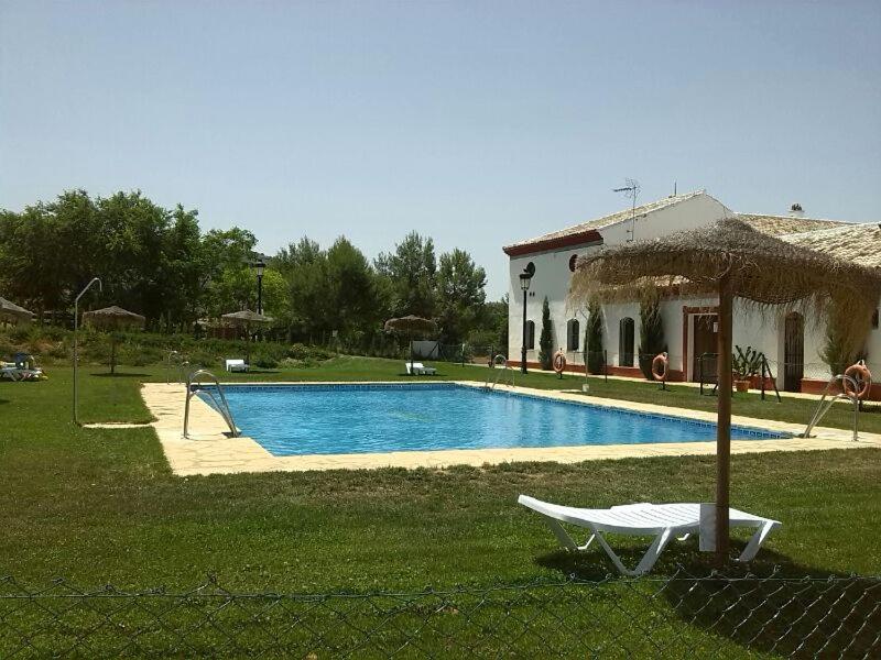 a swimming pool in front of a house with an umbrella at Complejo Pueblo Blanco in Olvera