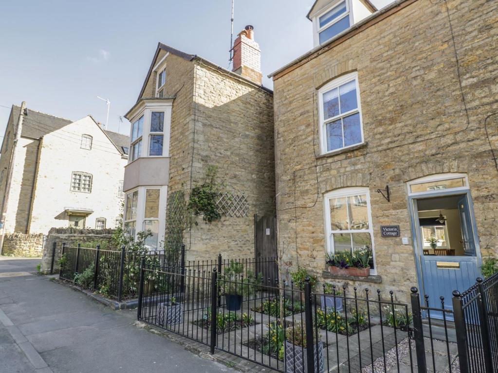 ein Backsteinhaus mit blauer Tür und einem Zaun in der Unterkunft Victoria Cottage in Chipping Norton