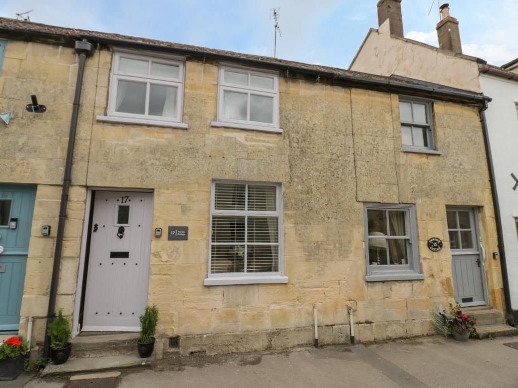 an old stone house with a white door and windows at Thimble Cottage in Cheltenham