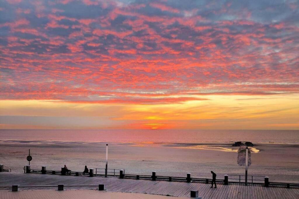 einen Sonnenuntergang über dem Strand mit Leuten, die auf einem Pier spazieren gehen in der Unterkunft Royal Palace Seaview Suite in Ostende