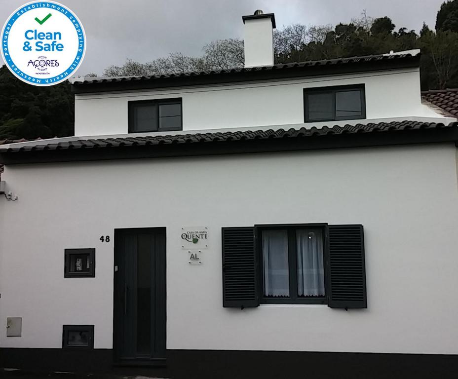 a white house with black windows and a blue sign at Casa da Água Quente 2 in Furnas