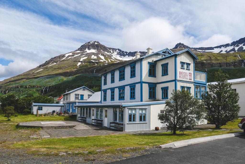 a large blue building with a mountain in the background at Hotel Aldan - The Post Office in Seyðisfjörður