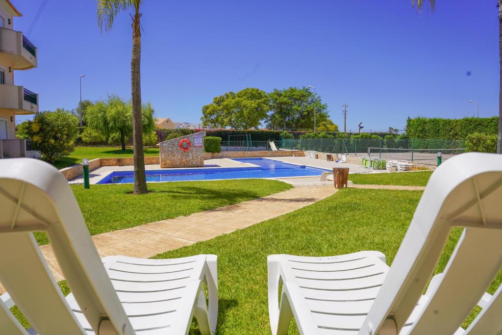 duas cadeiras brancas sentadas na relva perto de uma piscina em Kamaleon Sol by Sunny Deluxe em Albufeira