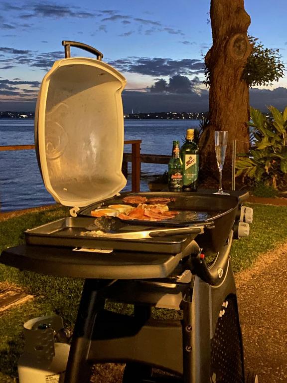 a grill with a pizza on it next to the water at Serenity by the Lake - Romantic Waterfront Couple's Getaway in Marks Point