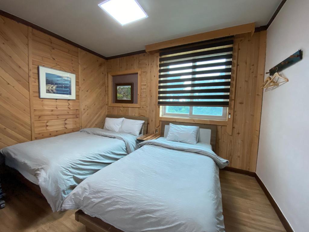 2 Betten in einem Zimmer mit Holzwänden und einem Fenster in der Unterkunft Smile Resort in Sokcho