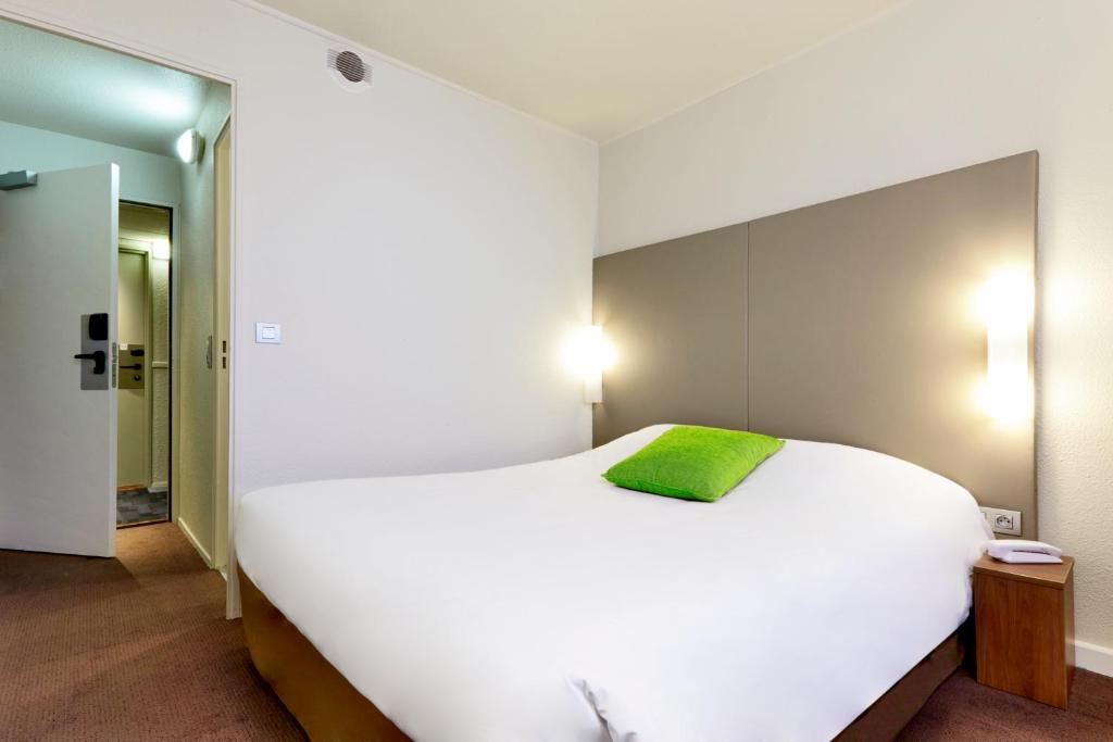 a bedroom with a large white bed with a green pillow at Campanile Paris Est - Porte de Bagnolet in Bagnolet