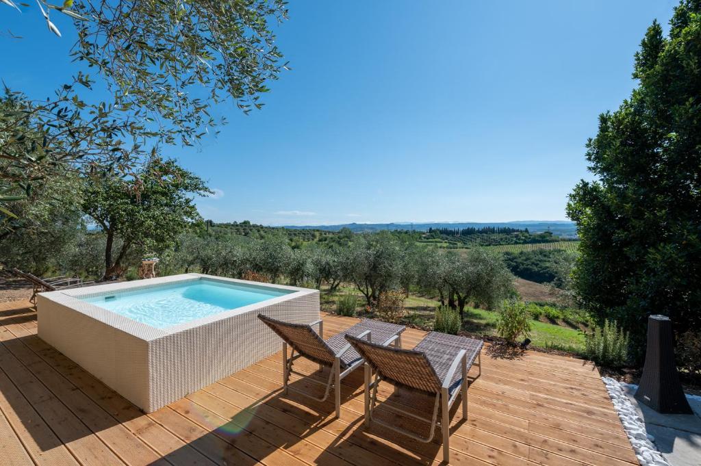 bañera de hidromasaje en una terraza de madera con 2 sillas en Il Leccio - casa toscana il fienile, en Gambassi Terme
