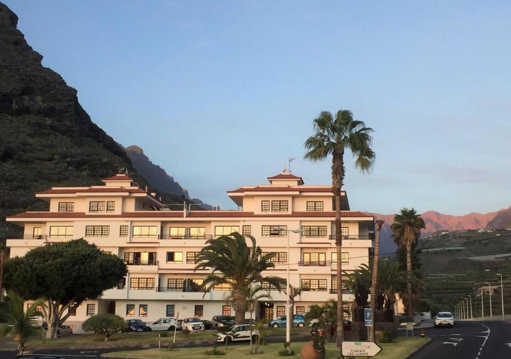 a large building with palm trees in front of a mountain at Apartamento Sol y Mar in Tazacorte