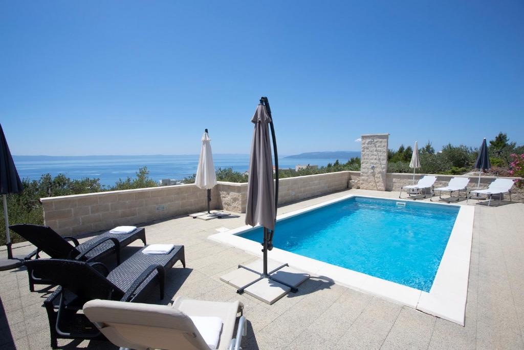 a swimming pool with chairs and umbrellas and the ocean at Villa Oaza in Makarska