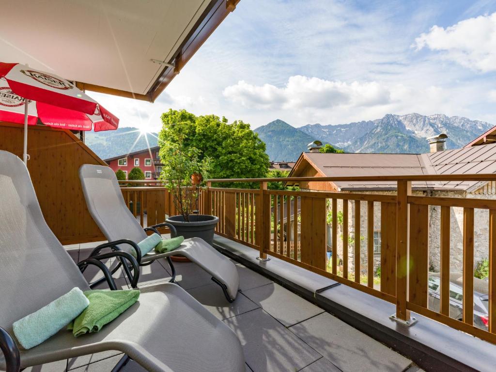 a balcony with chairs and an umbrella and mountains at Postgasthof Fischerwirt in Walchsee