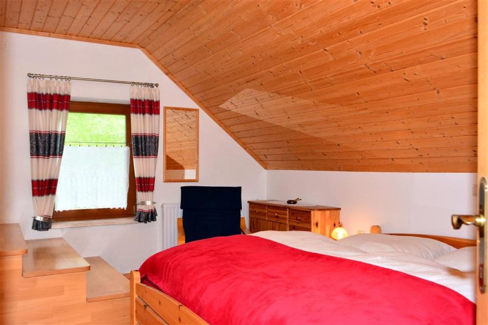 um quarto com uma cama vermelha e um tecto de madeira em Ferienwohnung Wieserberg em Dellach