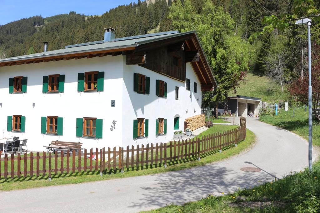 ein weißes Haus mit grünen Fenstern und einem Holzzaun in der Unterkunft Haus Monteiro in Elbigenalp