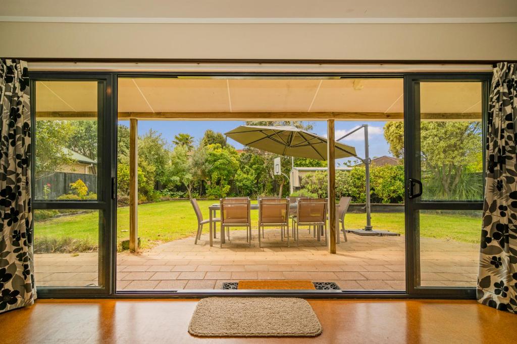 una puerta corredera de cristal con un patio con sombrilla en Kowhai Corner - Matarangi Holiday Home, en Matarangi