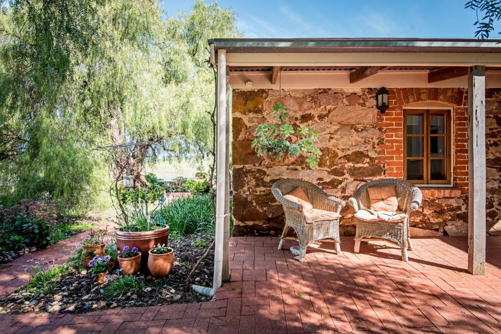un patio con 2 sillas de mimbre y una pared de piedra. en Lucy's Cottage, en Marananga