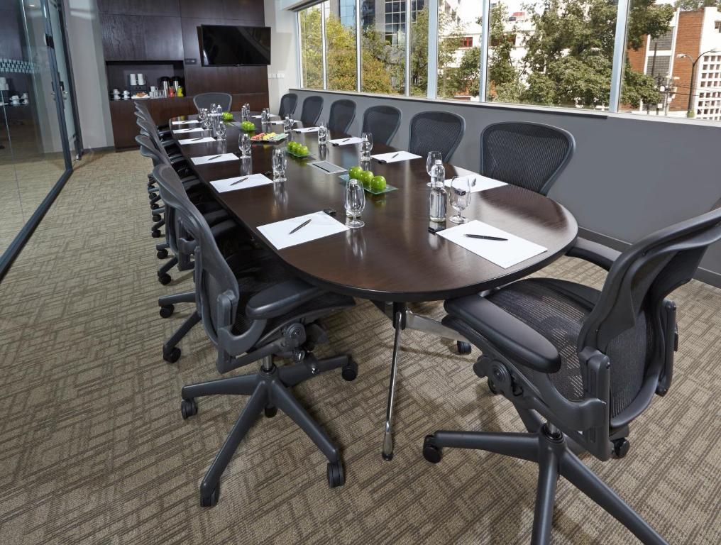 A bright conference room with a long meeting table, rolling chairs, and large windows.