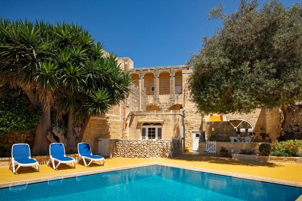 a swimming pool with two blue chairs and a building at Razzett Ghasri in Għasri